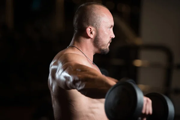 Muskulöses männliches Modell, das Schultern mit Kurzhanteln trainiert — Stockfoto