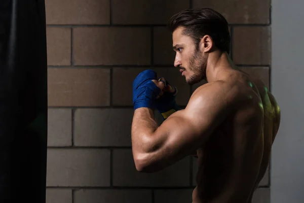 Shirtless boxer muscular com saco de perfuração no ginásio — Fotografia de Stock