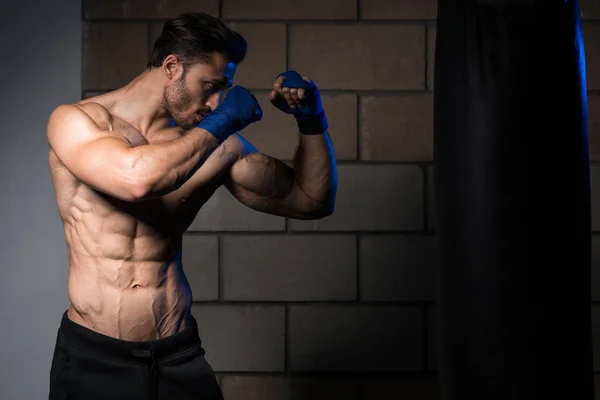 Shirtless boxer muscular com saco de perfuração no ginásio — Fotografia de Stock