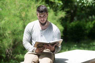 Genç Müslüman adam parkta Kur'an okuma