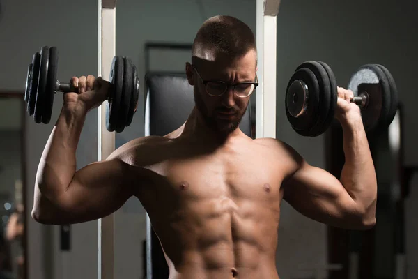 Homem muscular exercitando ombros com halteres — Fotografia de Stock