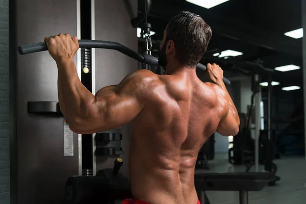 Homem muscular exercitando de volta na máquina de cabo — Fotografia de Stock