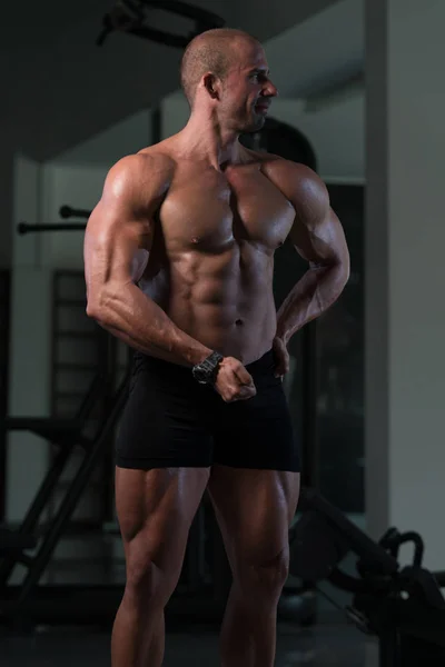 Fitness w kształcie mięśni mężczyzna pozowanie w ciemnym siłowni — Zdjęcie stockowe