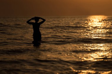 Kız gün batımında suda silüeti