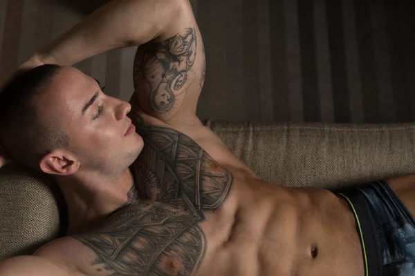 ソファに横たわるハンサムな上半身裸運動若い男 — ストック写真
