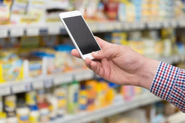 Człowiek przy użyciu telefonu komórkowego podczas robienia zakupów w supermarkecie — Zdjęcie stockowe
