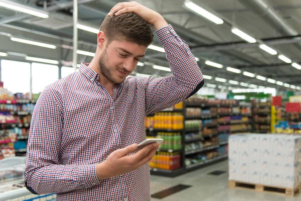 Człowiek szuka mylić na telefon komórkowy w supermarkecie — Zdjęcie stockowe