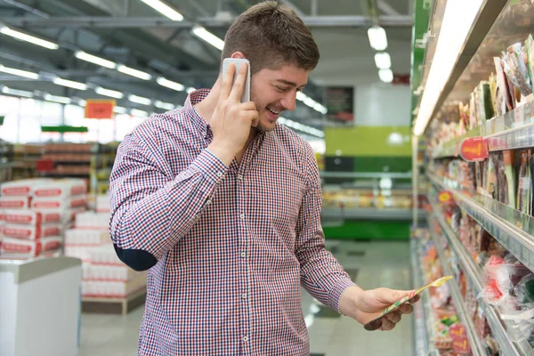 Süpermarkette cep telefonunda yakışıklı adam — Stok fotoğraf