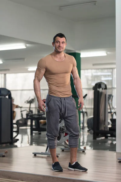 Hombre fuerte en camiseta marrón fondo gimnasio —  Fotos de Stock