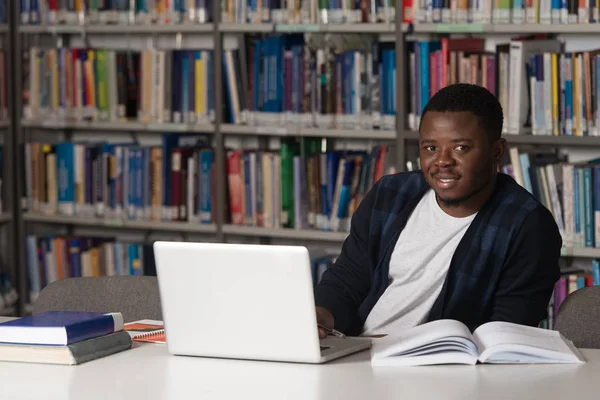 Jeune étudiant utilisant son ordinateur portable dans une bibliothèque — Photo