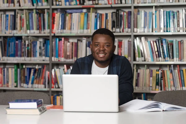 Heureux étudiant africain masculin avec ordinateur portable dans la bibliothèque — Photo