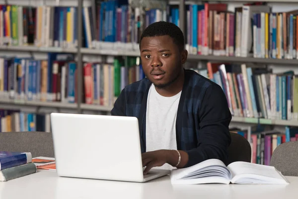 Jovem estudante usando seu laptop em uma biblioteca — Fotografia de Stock