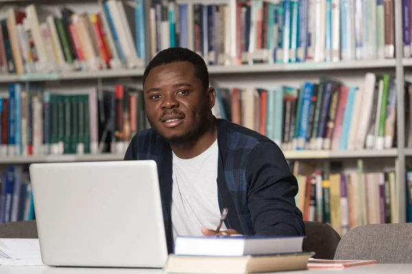 Jeune étudiant utilisant son ordinateur portable dans une bibliothèque — Photo