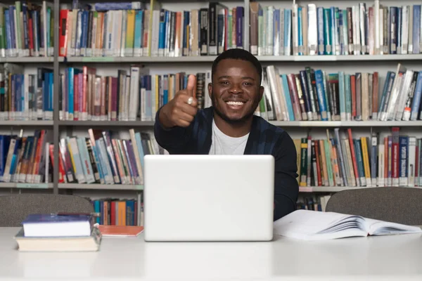 Estudiante africano en una biblioteca mostrando pulgares hacia arriba — Foto de Stock