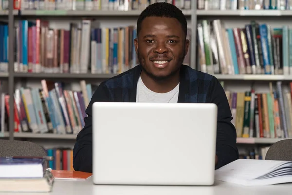 Jovem estudante usando seu laptop em uma biblioteca — Fotografia de Stock