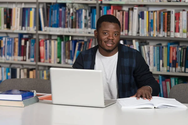 Jovem estudante usando seu laptop em uma biblioteca — Fotografia de Stock