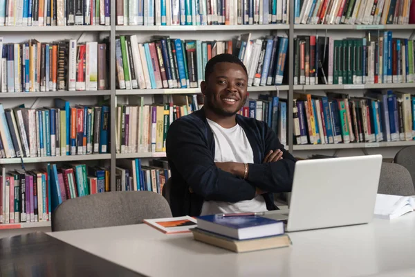 Щасливий африканський чоловік студент з ноутбуком в бібліотеці — стокове фото