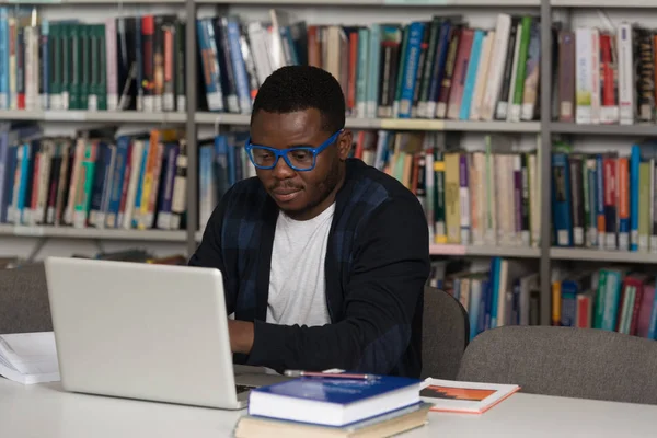 Счастливый африканский студент с ноутбуком в библиотеке — стоковое фото