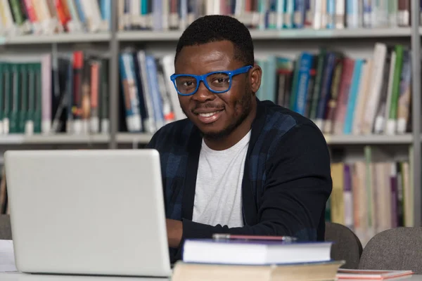 Jovem estudante usando seu laptop em uma biblioteca — Fotografia de Stock