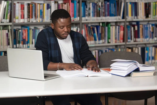 Νεαρός φοιτητής χρησιμοποιώντας το Laptop του σε μια βιβλιοθήκη — Φωτογραφία Αρχείου