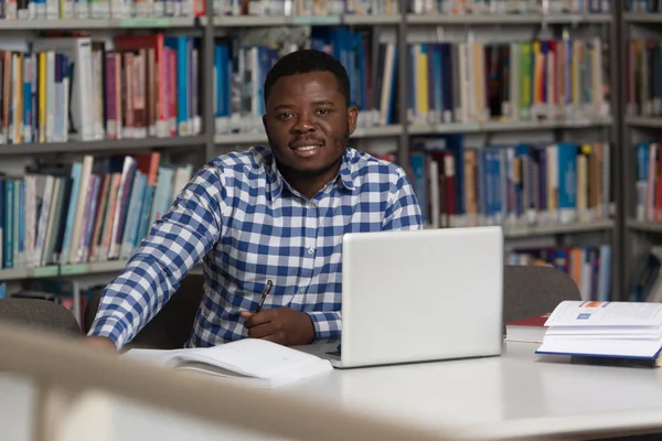 Jeune étudiant utilisant son ordinateur portable dans une bibliothèque — Photo