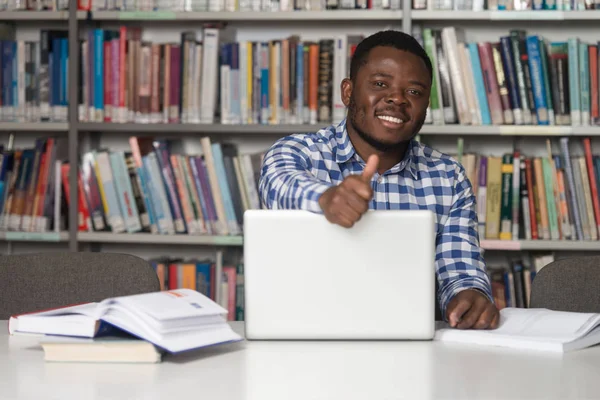 Estudante africano em uma biblioteca mostrando polegares — Fotografia de Stock