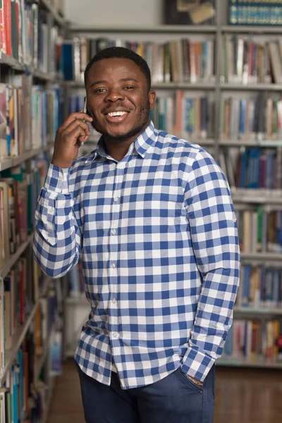 Hermoso estudiante universitario usando el teléfono móvil en la biblioteca — Foto de Stock