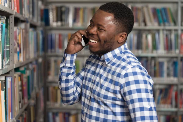 Étudiant beau collège utilisant le téléphone portable dans la bibliothèque — Photo