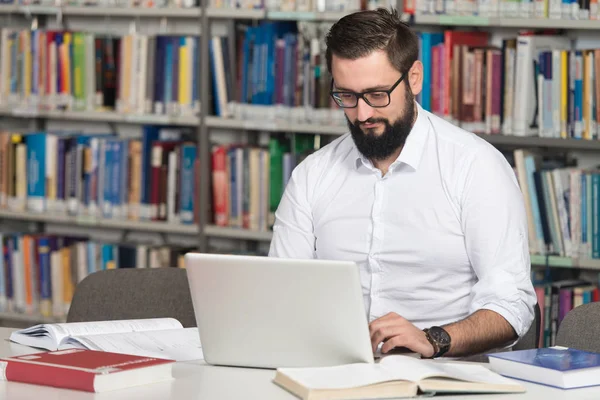 Feliz estudiante masculino con ordenador portátil en la biblioteca — Foto de Stock