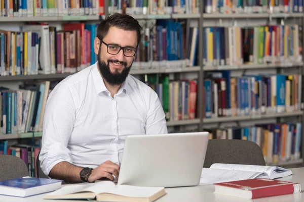 Glücklicher männlicher Student mit Laptop in Bibliothek — Stockfoto