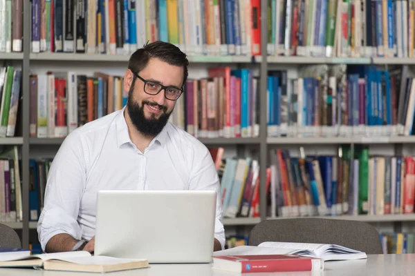 Feliz estudiante masculino con ordenador portátil en la biblioteca —  Fotos de Stock