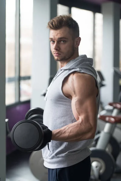 Fisiculturista exercitando bíceps com halteres no ginásio — Fotografia de Stock