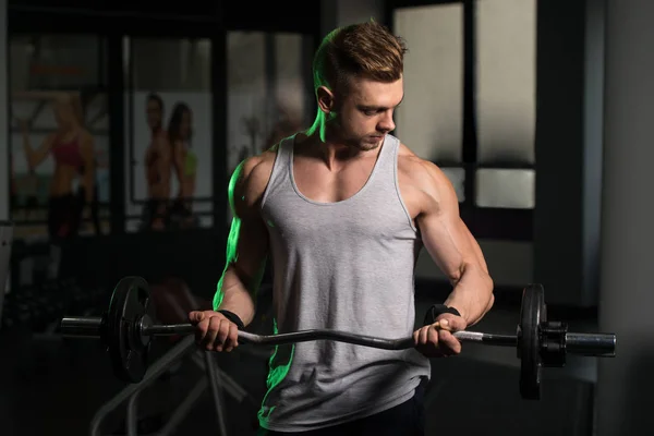 Culturista ejercitando bíceps con barra en el gimnasio —  Fotos de Stock