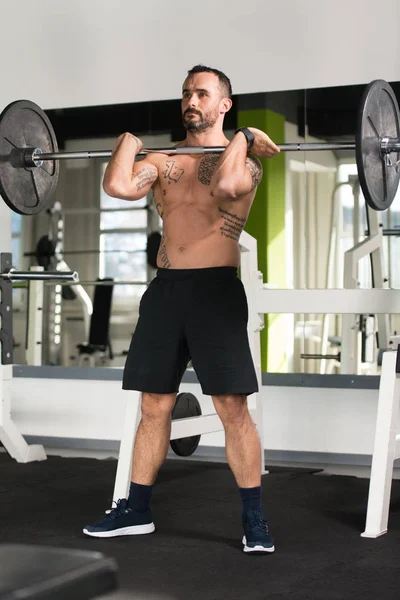 Fitness uomo utilizzando bilanciere ginnastica gambe dentro palestra — Foto Stock