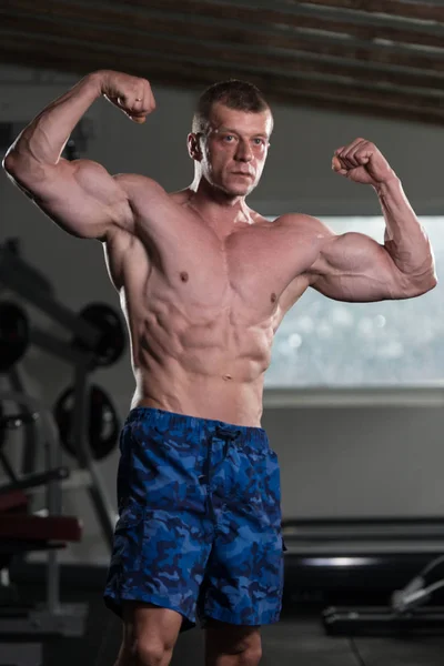 Musculoso hombre flexionando los músculos en el gimnasio — Foto de Stock