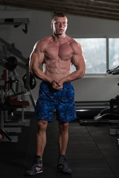 Hombre musculoso guapo flexionando músculos en el gimnasio — Foto de Stock