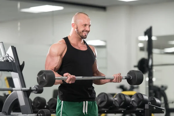 Hombre en el gimnasio ejercitando bíceps con barra — Foto de Stock