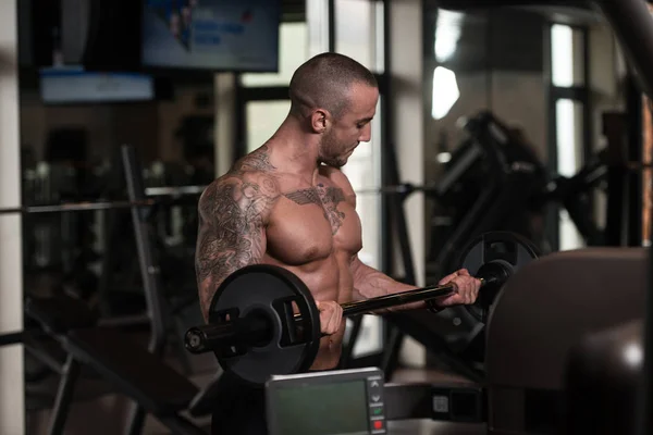 Hombre en el gimnasio ejercitando bíceps con barra — Foto de Stock