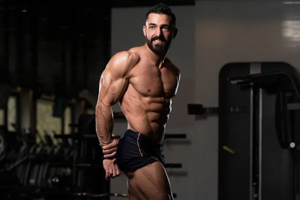 Hombre musculoso guapo flexionando músculos en el gimnasio — Foto de Stock