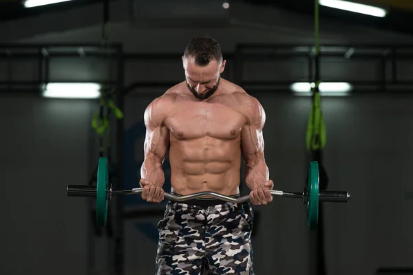 Hombre en el gimnasio ejercitando bíceps con barra — Foto de Stock