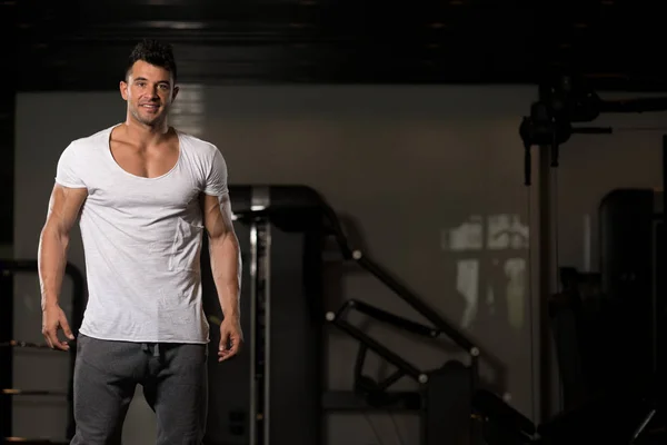 Hombre fuerte en camiseta blanca fondo gimnasio —  Fotos de Stock