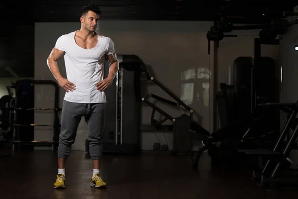 Hombre fuerte en camiseta blanca fondo gimnasio — Foto de Stock