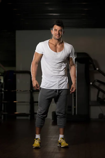 Hombre fuerte en camiseta blanca fondo gimnasio — Foto de Stock