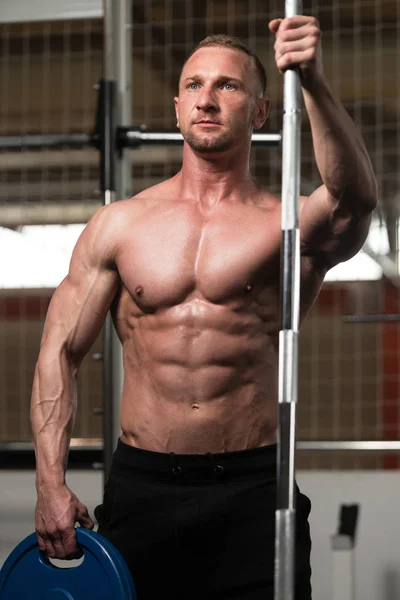 Bodybuilder lässt Muskeln mit Langhantel und Gewichten spielen — Stockfoto