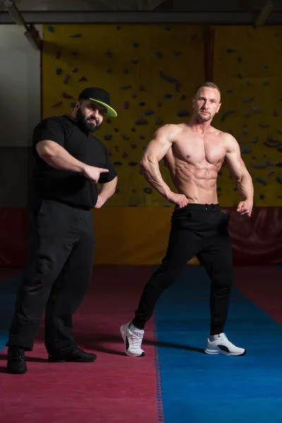 Man poserar Bodybuilding utgör och tränare rättar honom — Stockfoto