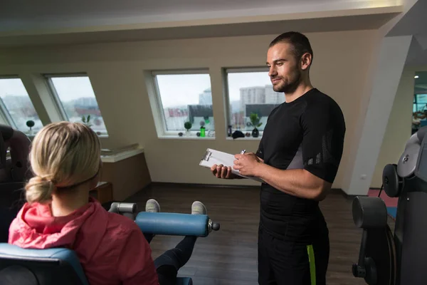 Entraîneur personnel prend des notes pendant que la femme exerce jambes — Photo