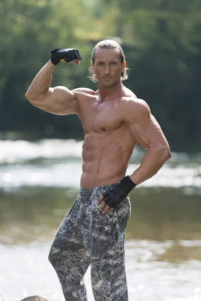 Bodybuilder buigen spieren buiten In de natuur — Stockfoto