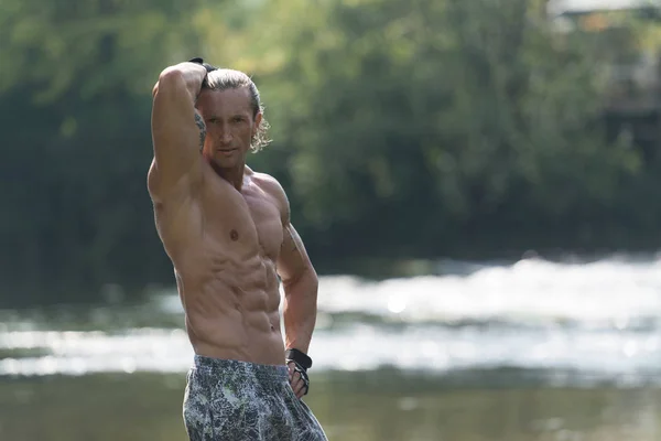Schöner schleimiger Mann, der draußen in der Natur Muskeln spielen lässt — Stockfoto
