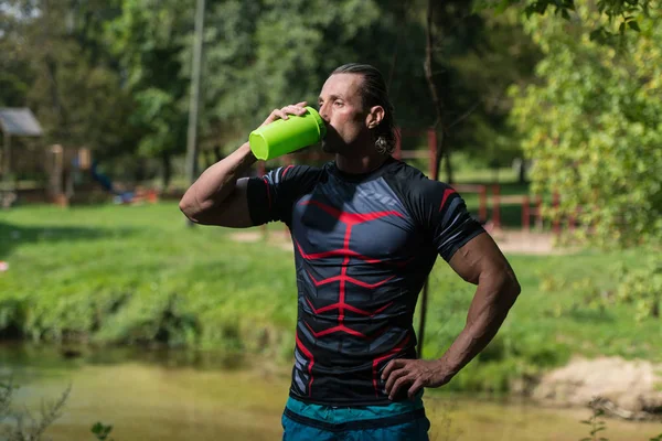 Bodybuilder drinkwater uit de Shaker buiten In de natuur — Stockfoto