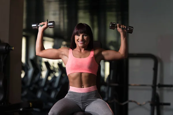 Mulher exercitando ombros com halteres no ginásio e flexing — Fotografia de Stock
